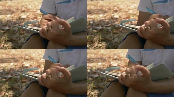 夏天，在公园的树荫下，女人坐着和写作的手在日记中激发生活。户外工作录音。