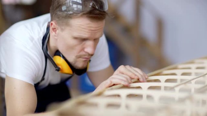 聚焦中年木匠在木工车间工作台上建造木船模型的特写跟踪镜头