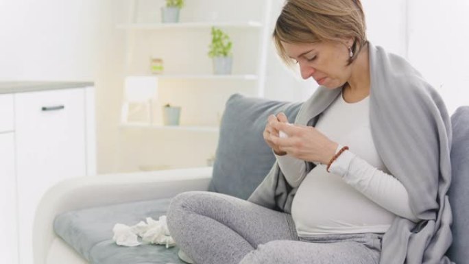 孕妇感冒，流感，病毒，坐在家里的沙发上，吹鼻子和生病。