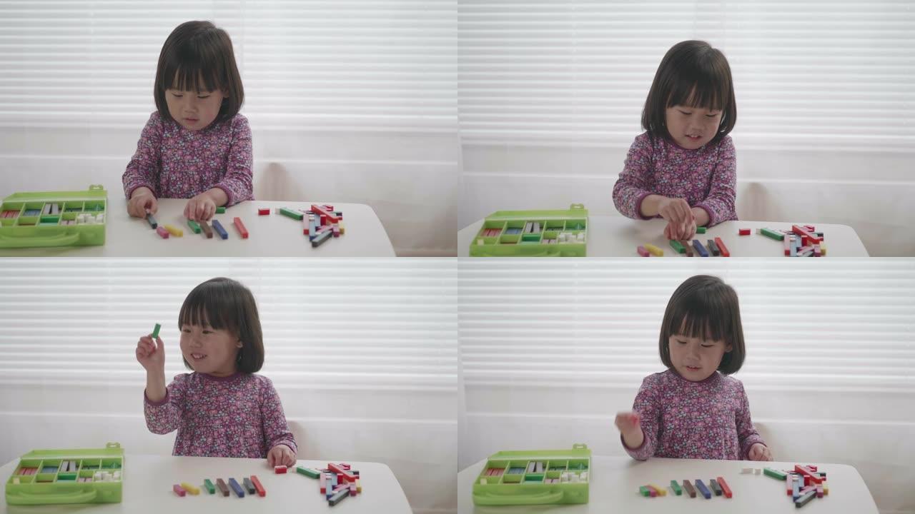 蹒跚学步的女孩在白色窗户背景下的桌子上玩形状玩具块