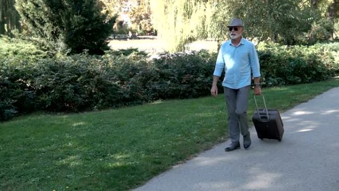 老人带着行李穿过公园