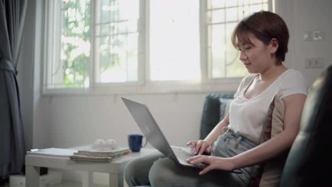 年轻的亚洲妇女坐在家里用笔记本电脑工作