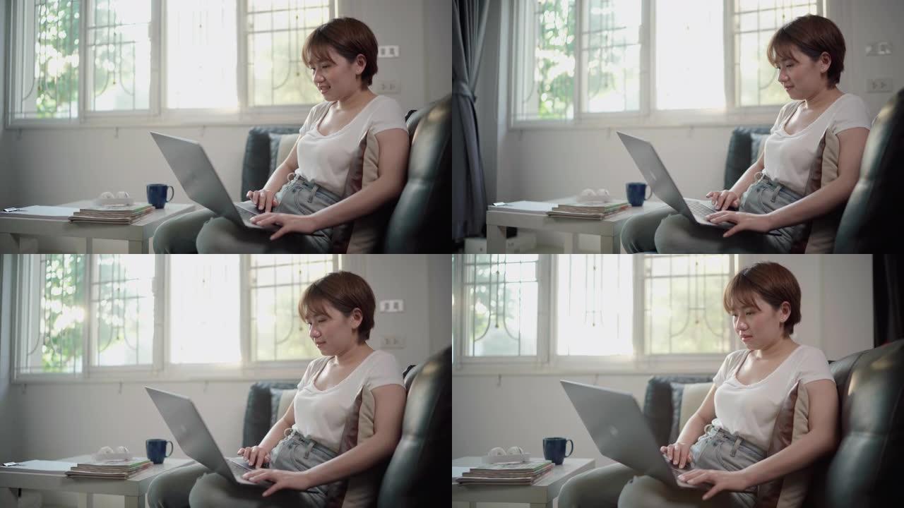 年轻的亚洲妇女坐在家里用笔记本电脑工作