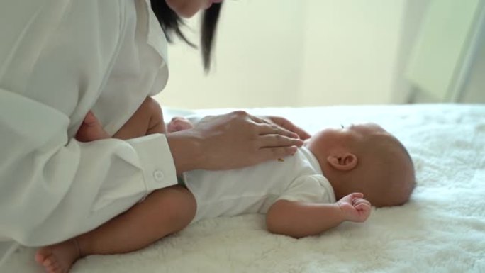 可爱的新生男婴躺在床上，母亲在室内把手放在肚子上。年轻的亚洲母亲在卧室里抚摸婴儿