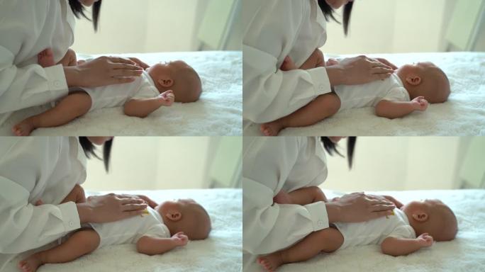 可爱的新生男婴躺在床上，母亲在室内把手放在肚子上。年轻的亚洲母亲在卧室里抚摸婴儿