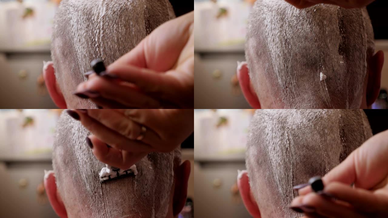 女人的手用剃须泡沫和剃刀剃男人的头的特写镜头。