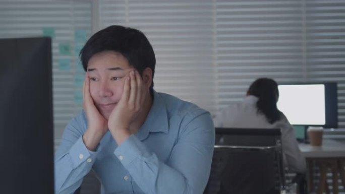 疲惫的亚洲男工在公司办公室里用台式电脑工作