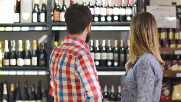 恋爱中的白人年轻夫妇在商店中选择豪华葡萄酒的后视图。男人和女人站在架子前喝酒，互相看着对方，微笑着，