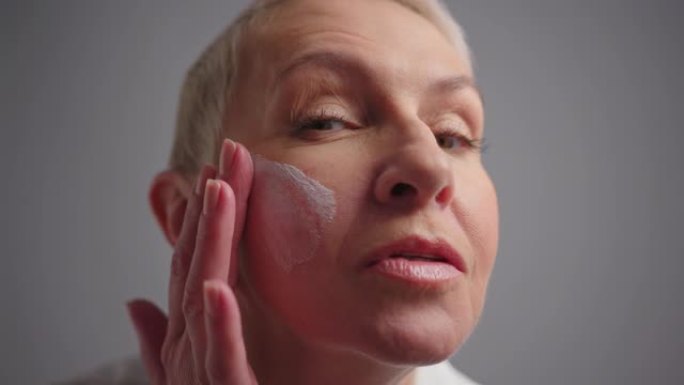 老年妇女在颧骨上涂抹面霜，打圈涂抹面霜，护肤，天然化妆品，面部护理