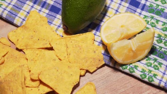 在柠檬和鳄梨的背景下，将咸玉米片玉米片倒在木桌上。美味有害零食，快餐4k
