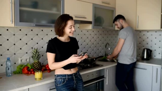 美丽的年轻夫妇在家里的厨房里烹饪健康食物时说话和微笑