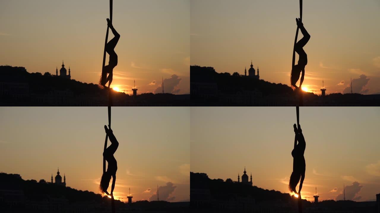 基辅城市背景日落时，空中丝绸上灵活的女杂技演员的剪影。自由与和平的概念