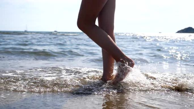 女性的脚在海滩上的海水上行走，海景和波浪背景。年轻女子沿着海岸行走的腿。赤脚女孩漫步在海边。暑假或旅