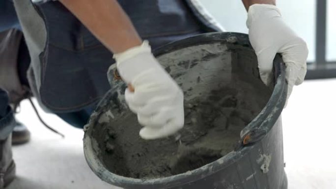 4k关闭高级杂工手使用抹刀在桶中搅拌混凝土水泥砂浆，用于准备家庭装修维修施工或瓷砖铺路。高级杂工di
