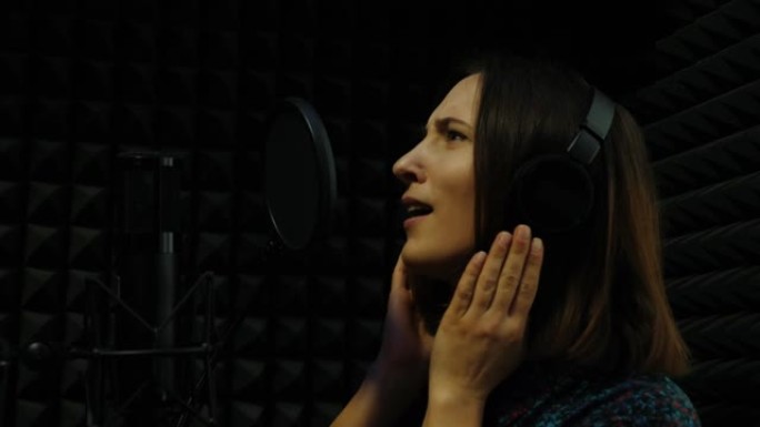 年轻的女歌手在专业录音室用麦克风唱歌。戴着耳机的女人在声音音乐工作室录制这首歌。家庭音乐录音棚概念