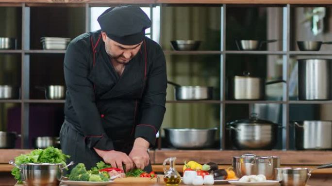 穿着黑色制服的英俊男厨师切青菜和胡椒。红色相机上的中等镜头
