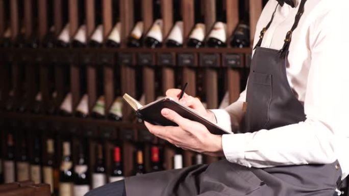男性葡萄酒管家在葡萄酒商店里看着几瓶酒并在笔记本上写字