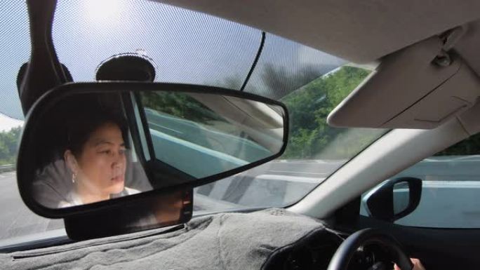 在道路上行驶时车内后视镜上的反射亚洲女司机