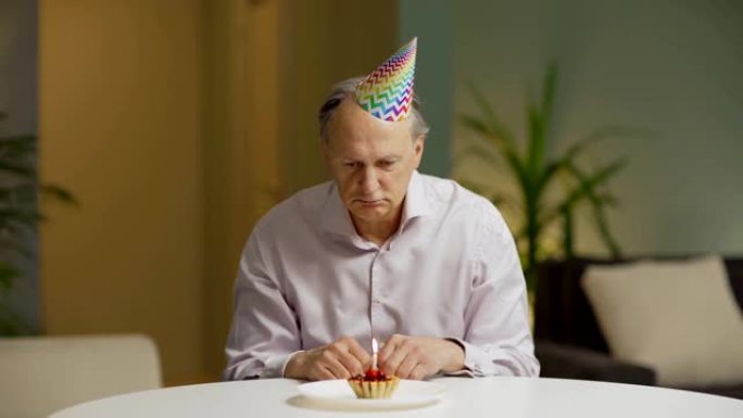 Unhappy senior man in party hat sitting alone at t