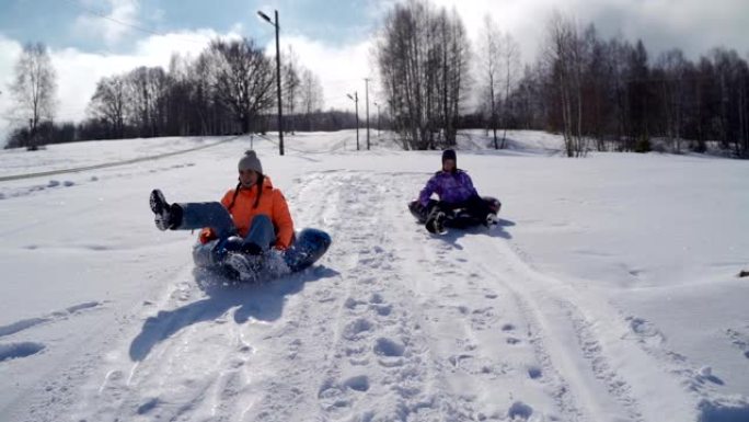 两个女孩在山上雪橇。冬季寒冷时间