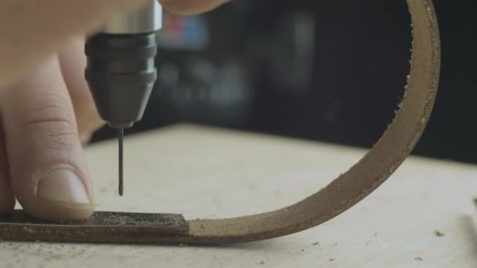 皮革工匠用钻头在皮革表带上钻孔的特写镜头。手工制品。电影院4k视频。C4k