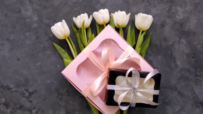 白色郁金香花与黑色和粉红色礼品盒在黑暗背景平躺着。4k视频顶视图。3月8日快乐女性母亲节概念。花束，