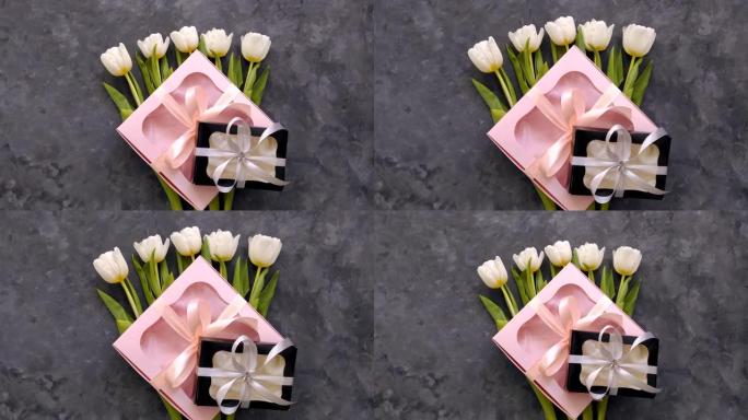 白色郁金香花与黑色和粉红色礼品盒在黑暗背景平躺着。4k视频顶视图。3月8日快乐女性母亲节概念。花束，
