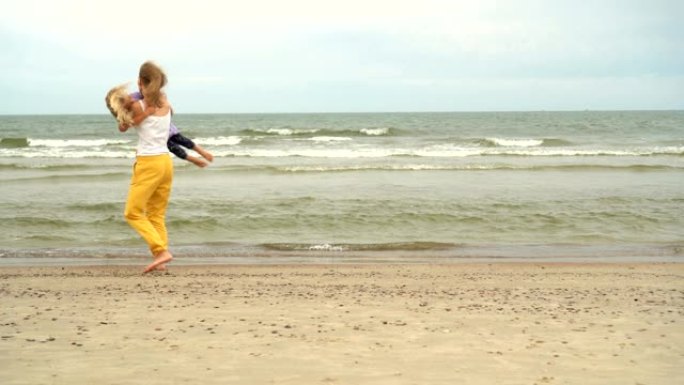 女儿跑向妈妈，在海滩上拥抱拥抱。母亲举起女孩的手