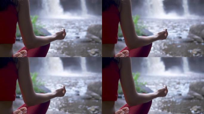 关闭亚洲女子在瀑布练习或做瑜伽，莲花在冥想环节摆姿势。美丽的风景，自然的背景，泰国。