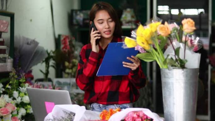 亚洲女花店小商花店老板，她正在用电话和笔记本电脑为她的商店下订单。