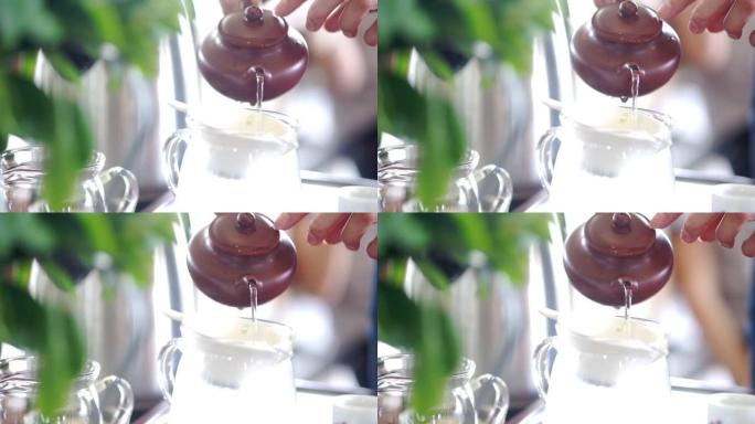 双手将陶瓷茶壶中的热水倒入玻璃茶壶中，用于制作热茶。