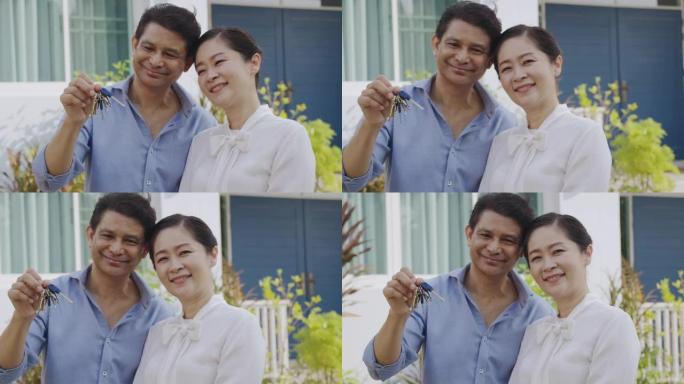 高级夫妇肖像在他们的房子前面拿着房子钥匙。快乐时刻。面对镜头。慢动作。50多岁的亚洲男女。