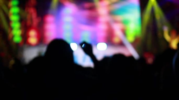 慢动作，人们在大厅舞台前的摇滚音乐会上聚会，欢呼和示手的剪影。彩色蓝色舞台灯光，带发光二极管灯的舞台