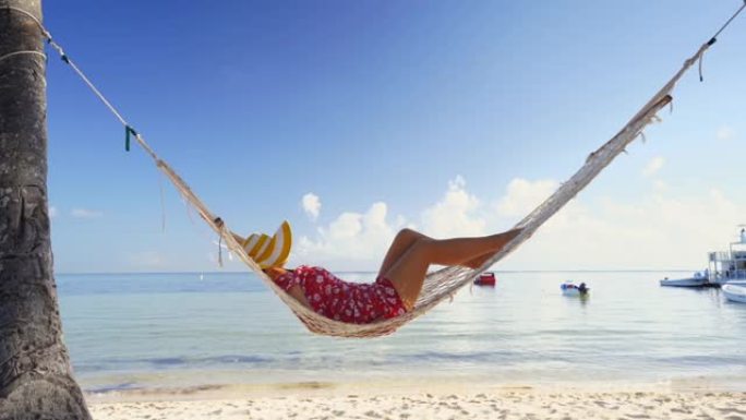 女孩在热带岛屿海滩的吊床上放松。多米尼加共和国蓬塔卡纳的暑假