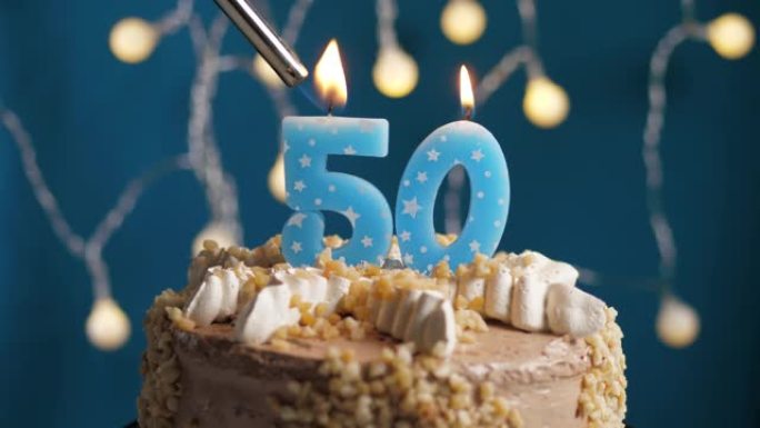 蓝色背景上有50号蜡烛的生日蛋糕。蜡烛着火了。慢动作和特写视图