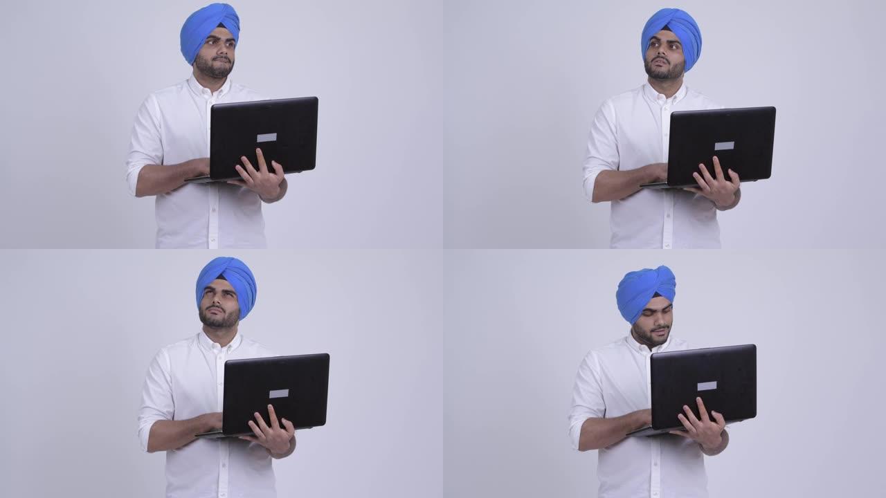 年轻的大胡子印度锡克教徒在使用笔记本电脑时带着头巾思考