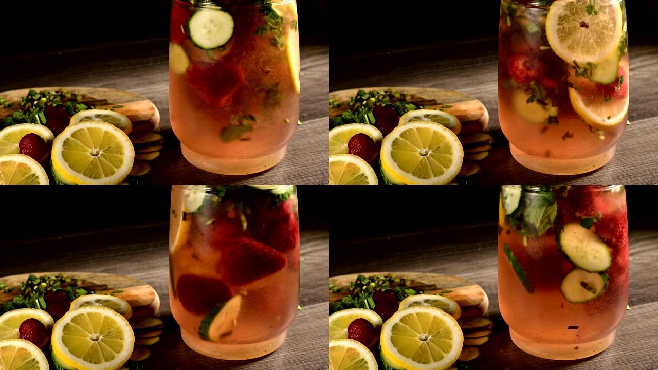 玻璃水瓶中的特写镜头是柠檬片和黄瓜，薄荷和冷冻草莓在苏打水中搅拌。在柠檬水玻璃器皿中旋转水果