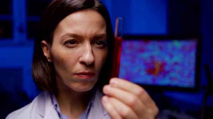 放大集中的中年女化学家的特写镜头，仔细检查实验室中红色液体的试管