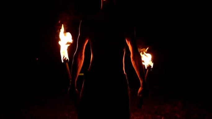 一个穿着黑色裤子的年轻人在完全黑暗中的特写慢动作显示了旋转的火炬的代表。运动中的冥想。冷静而坚定不移