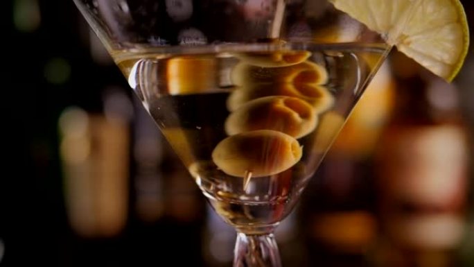 马提尼酒杯的特写镜头，橄榄在酒瓶上缓慢旋转。