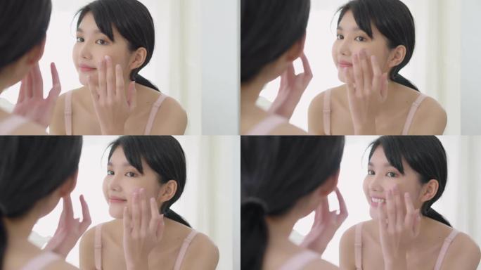 美丽的年轻亚洲女人微笑着看着镜子检查面部和护肤霜和化妆品的年轻化和卫生，美容女孩快乐清洁面部乳液和健