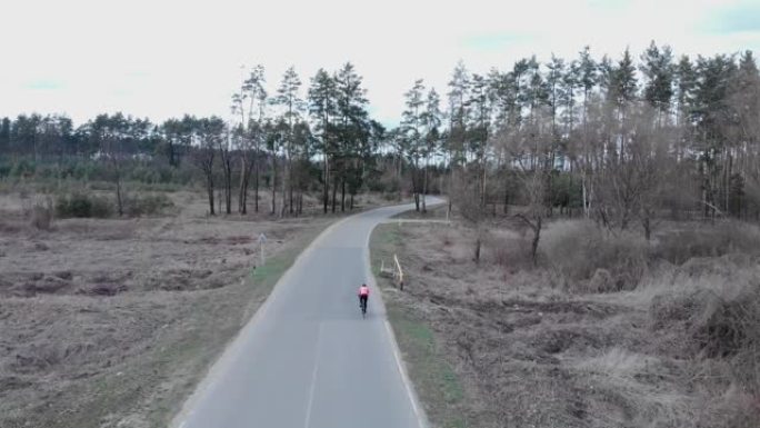 骑自行车的人在松树森林空旷的高速公路上快速密集地踩着公路自行车。运动员独自骑自行车艰苦训练的鸟瞰图。