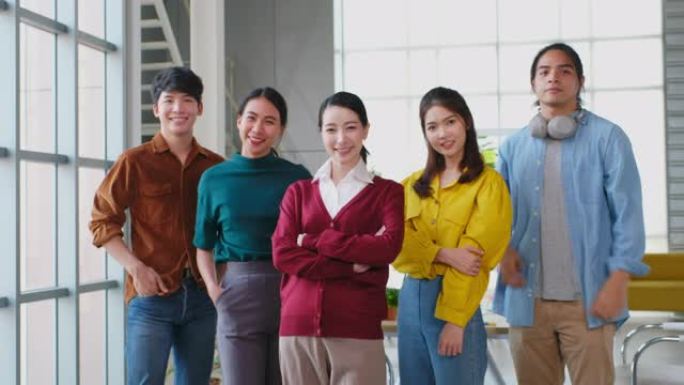 亚洲商业快乐的肖像，创意企业家团队微笑着看着现代办公室里的相机，一群亚洲年轻人的团队合作伙伴关系站在