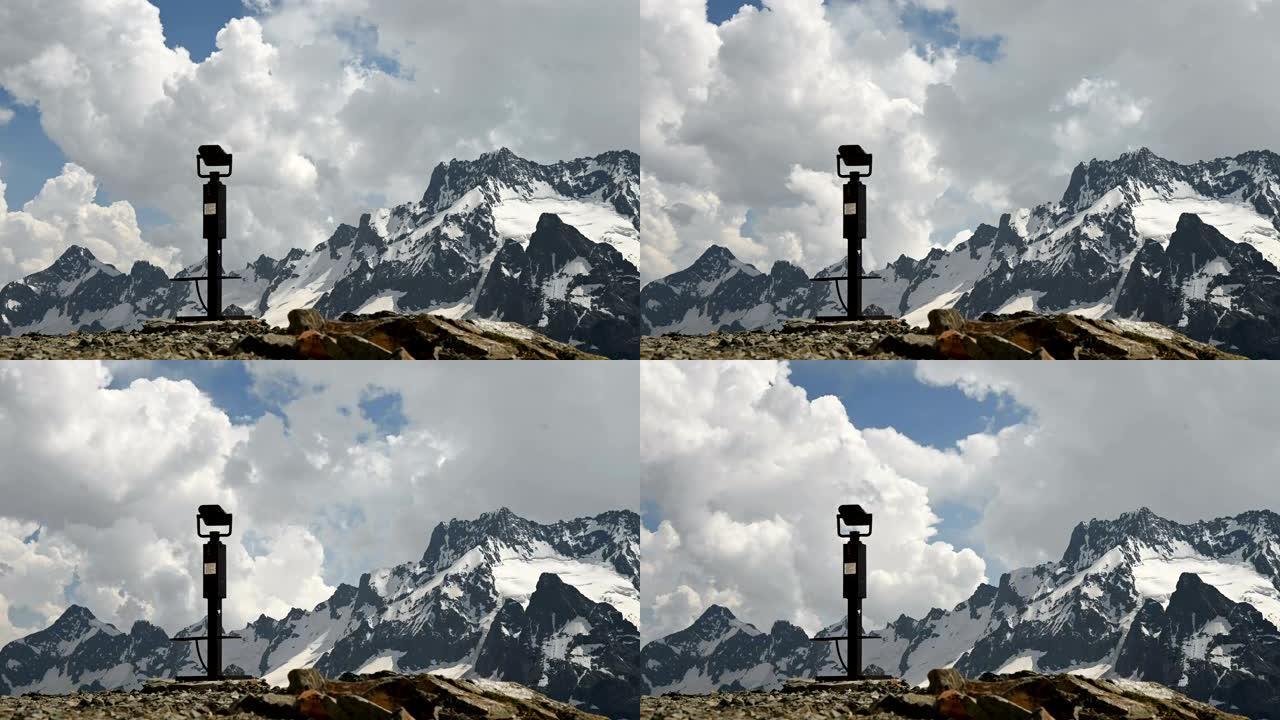在天气变化之前，在白雪皑皑的岩石高山和积云的背景下观看固定双筒望远镜