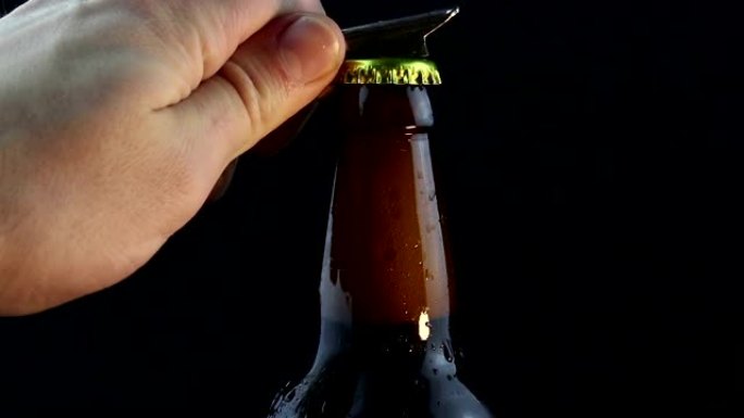 酒保打开一瓶迷雾的黑啤酒。一个年轻人的手打开一瓶冷的黑啤酒。