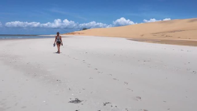 走在白色沙滩上的女人留下脚印