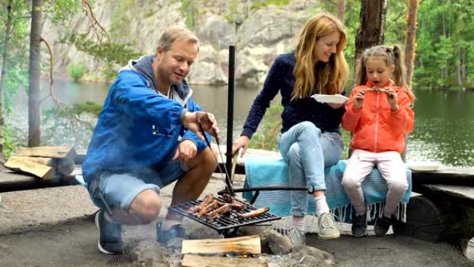 一对夫妇带着一个孩子在湖岸的森林里烧烤