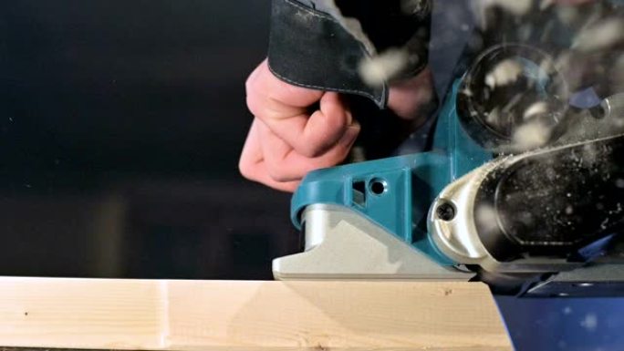 大特写。木匠用电动飞机切割木板。尘埃颗粒和锯片的慢动作