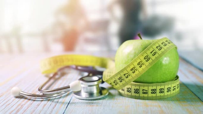健康的生活方式和营养-苹果在健身房的桌子上有测量胶带和听诊器，背景是跑步的人