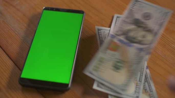 男人在桌子上的手机屏幕触摸板旁边折叠百美元钞票。绿屏手机模型。货币现金色度关键概念。技术和经济。个人